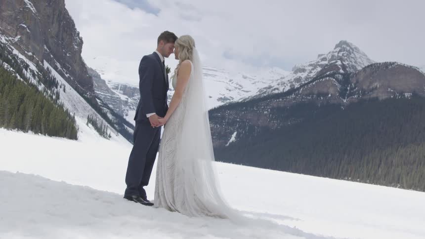 A bride and groom stand face to face as the pose outdoors in front of a winter landscape with forests and mountains