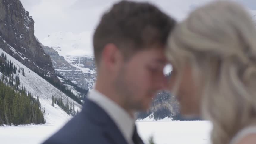 A bride and groom embrace with snowy mountains in the distance