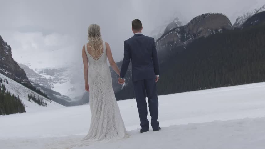 A bride and groom stand in the snow in the valley of a mountain