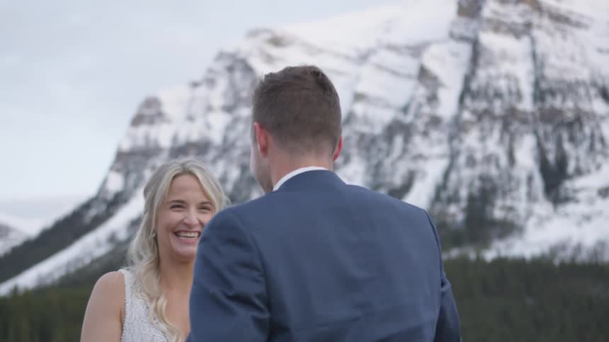 Wedding couple hugging under snowy mountain