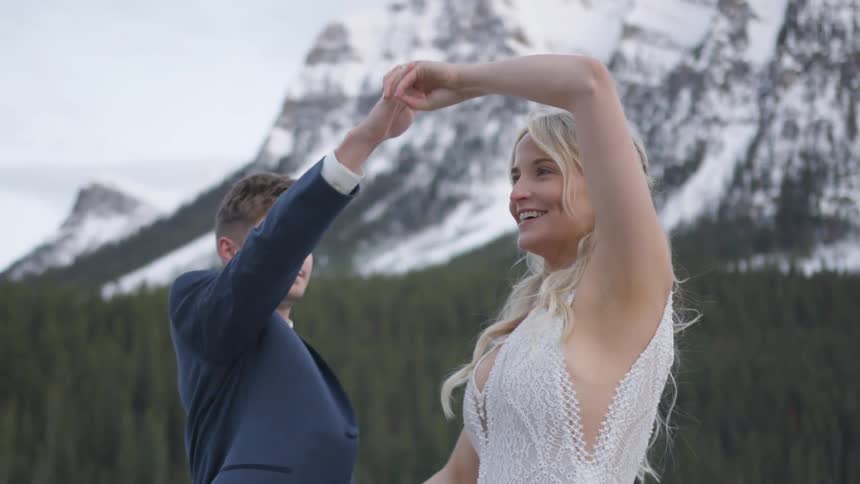 A bride and groom dance beside snow covered mountains