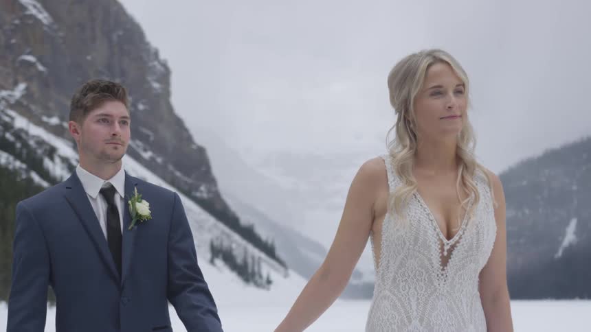 A bride and groom walk through a snow covered canyon