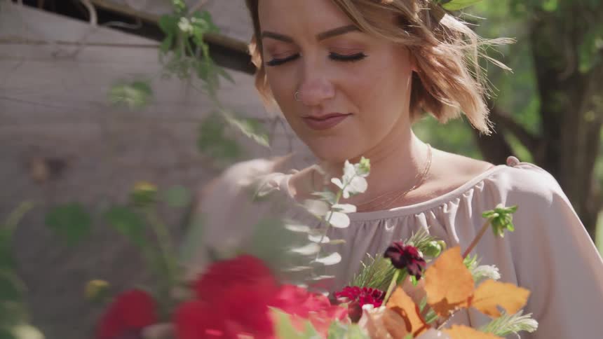 A woman stands outside with her eyes closed holding a bouquet of flowers