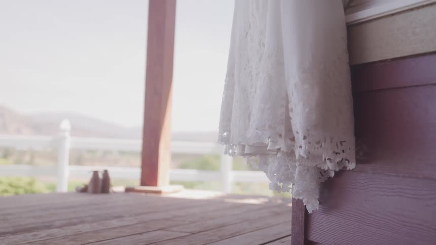 Hem of a wedding dress hanging outside by a window on the porch