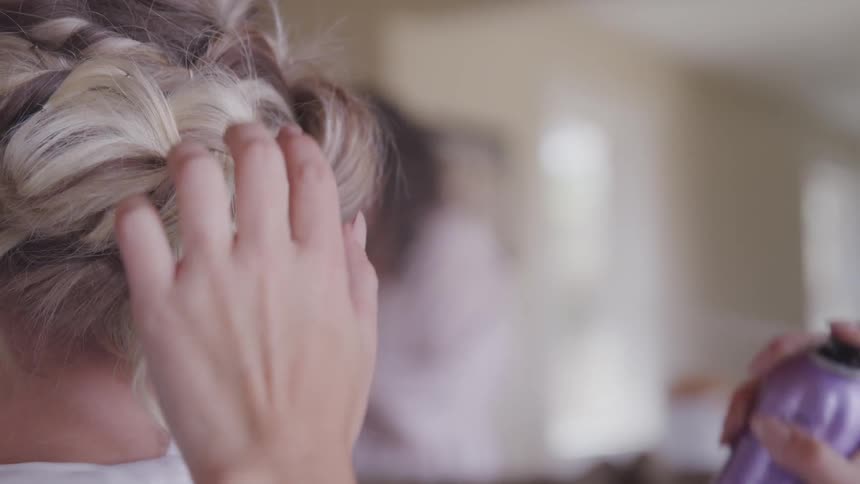 A woman uses hairspray on another womans hairstyle