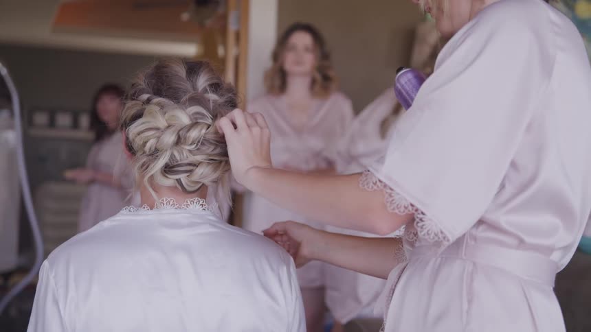 A seated woman in a robe is having her hair styled as several other women in identical robes look on