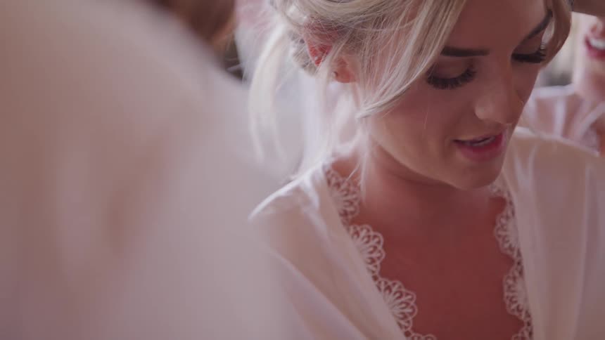 A blonde haired woman in a white robe sits while someone styles her hair