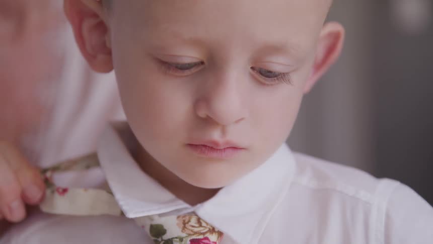 A woman puts a tie on a little boy