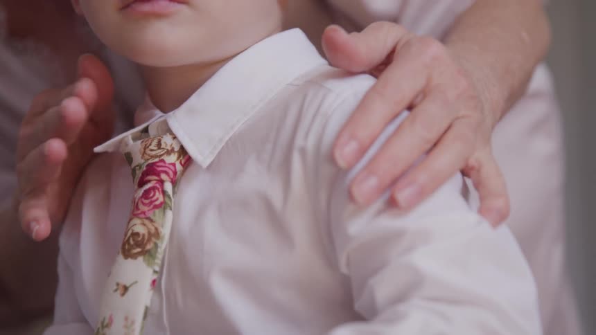 A woman fixing a tie on a boy while he holds a hanger and a green poker chip