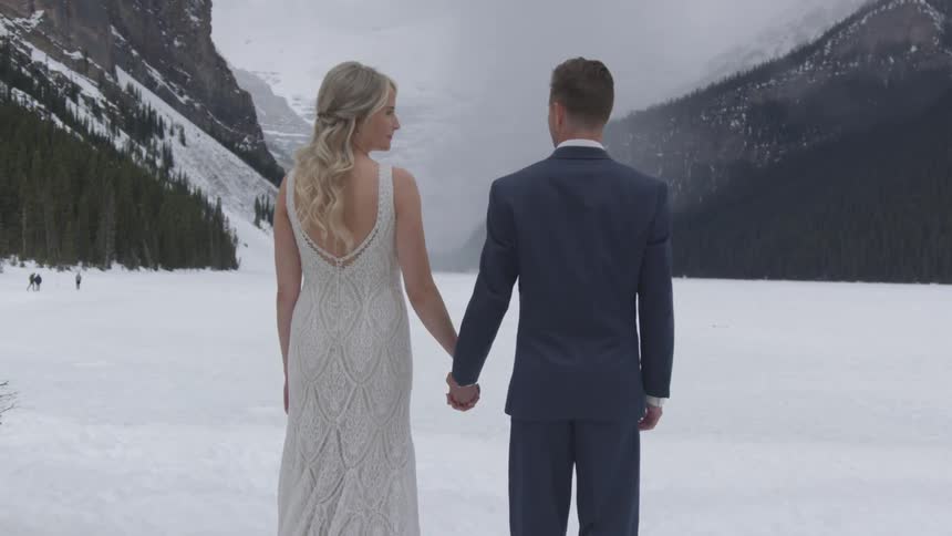 A wedding couple looks out over a frozen lake and then towards each other