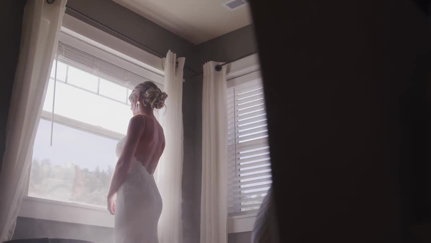 Woman in wedding gown in a room looking through a window