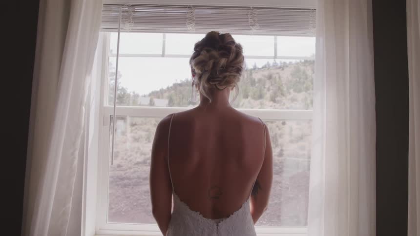 Woman in wedding dress posing looking out a window