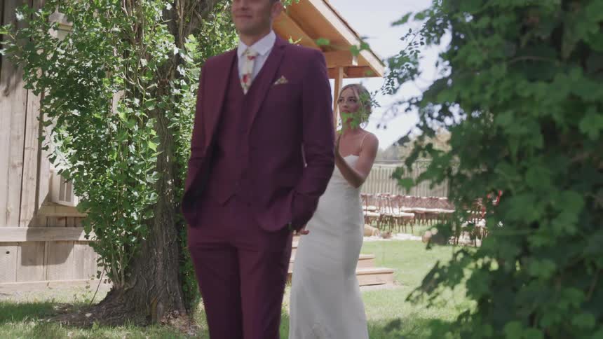 A bride walks up behind her groom who is not looking towards her