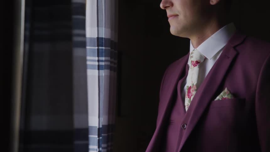 Groom stands and looks out the window in a room