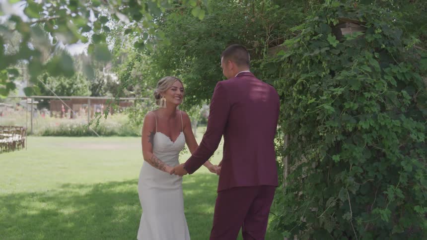 A bride and groom hold hands as they smile while standing outside in a garden area