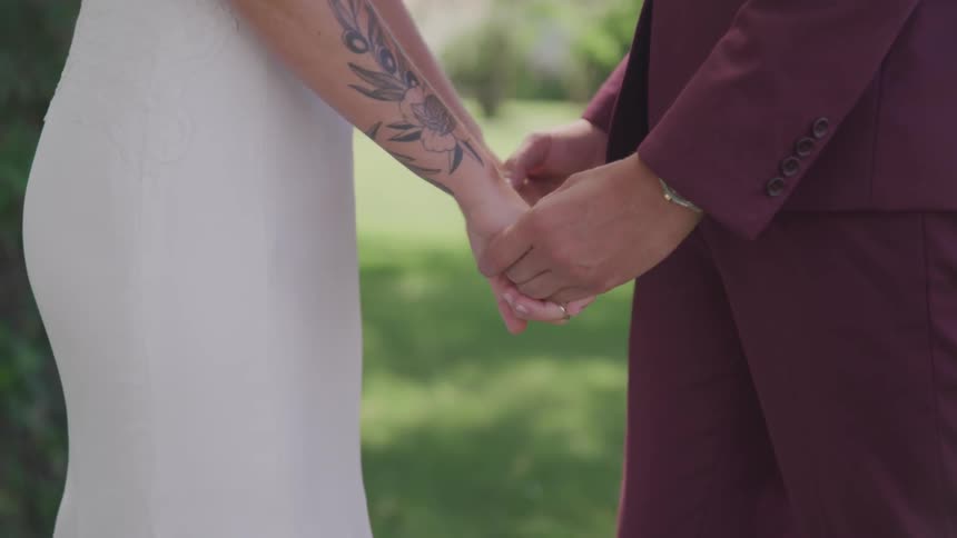 A couple in a suit and wedding dress hold hands outside