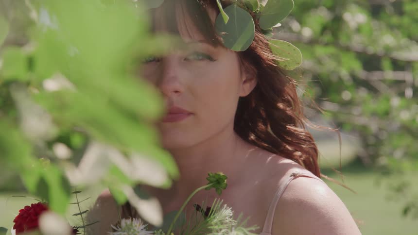 A young woman holding a bouquet of flowers looks off in to the distance