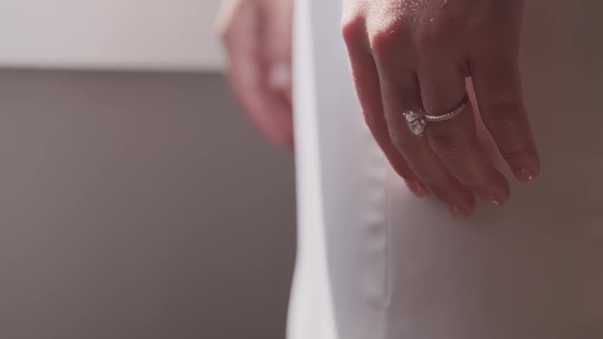 A bride stands and poses with her hand and wedding ring to her side