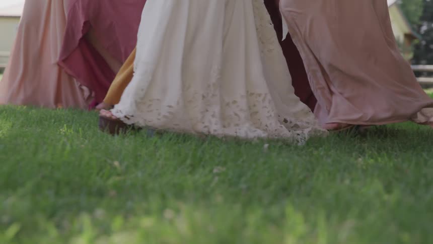 Bride and bridesmaids with gowns and dresses walking on grass