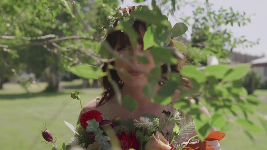 A woman stands behind a tree branch while holding a bouquet of flowers