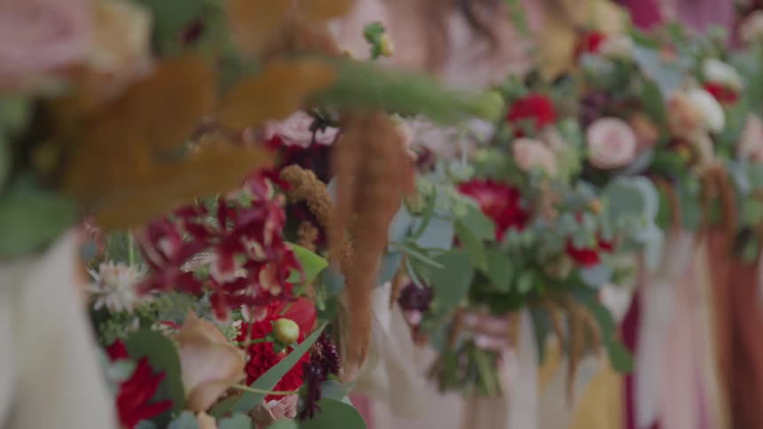 The wind blows the ribbons on a row of bouquets held by bridesmaids in colorful gowns