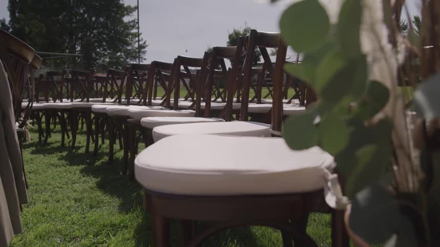 Rows of chairs lined up on grassy field near trees under sunny clear sky