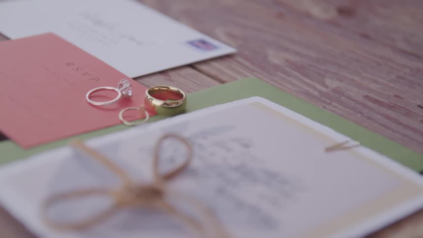 A postcard envelope and invitation under a pair of rings on a wooden table