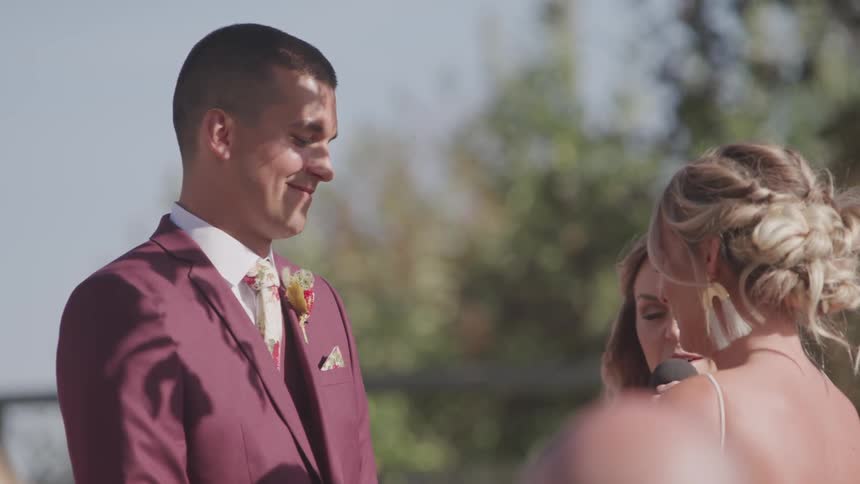 Bride dries her eyes with a tissue as the groom is smiling at her and then turns his head to look at the officiant talking in front of them