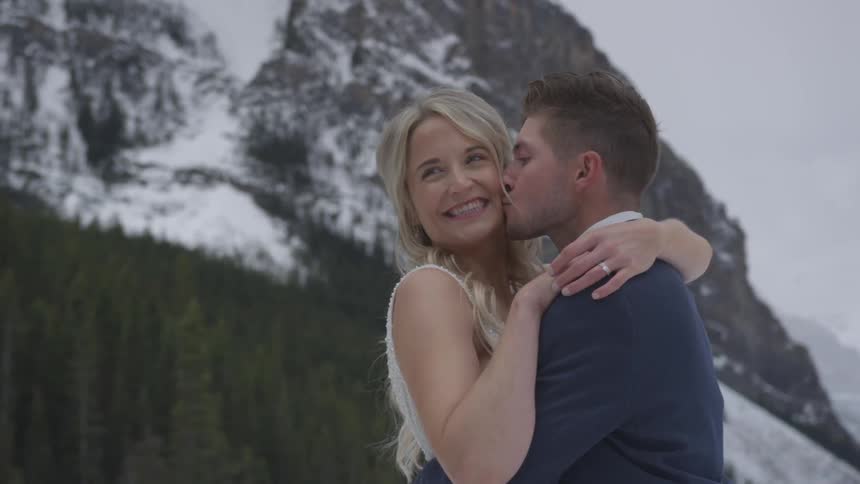 Newlyweds kissing and embracing in front of snow covered mountain