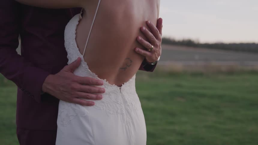 Groom touches the brides back on the grass during the wedding ceremony