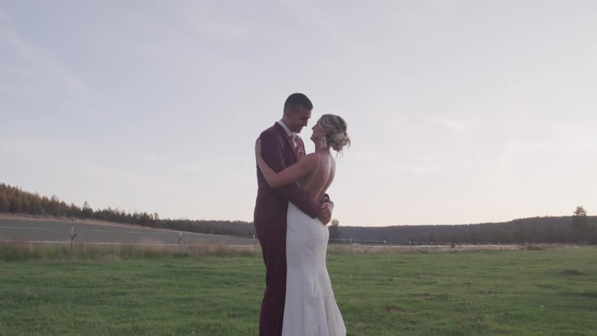 A bride and groom hold each other in a large grassy field