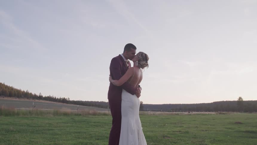 A groom and bride kissing in the middle of a grass land