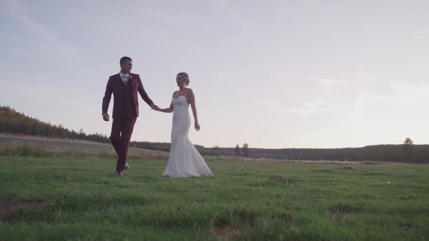 Bride and groom gaze into each others eyes as they walk hand in hand through a grassy field