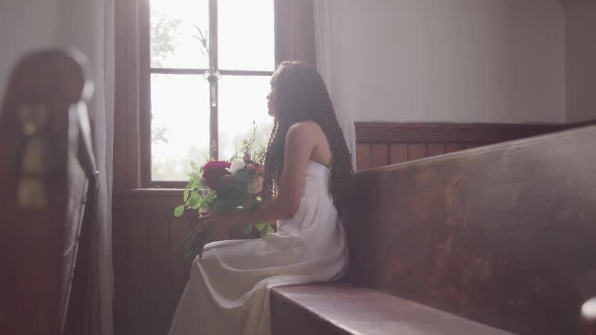 A female groom with a bouquet looking outside from the window