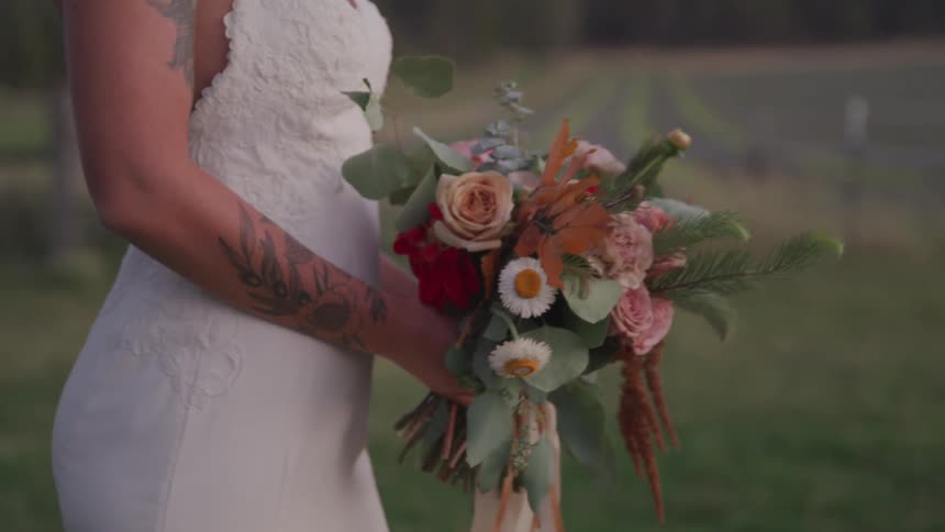 A bride walks across a field holding a bouquet