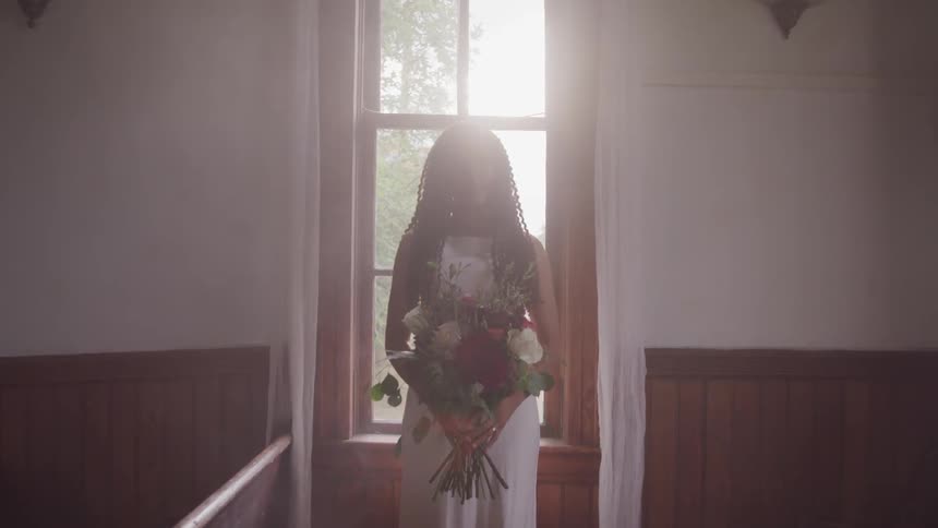 Black bride holding a bunch of flowers stands before the window in the church