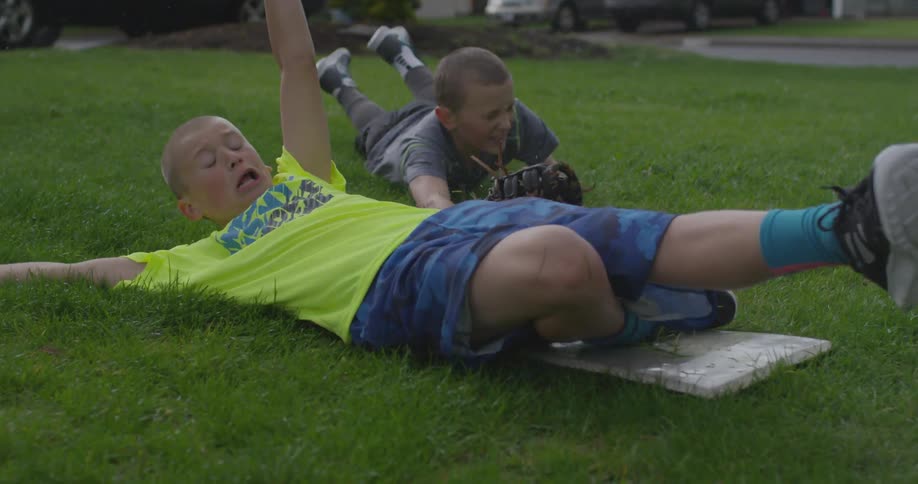 Two kids slide towards a base on a sunny day