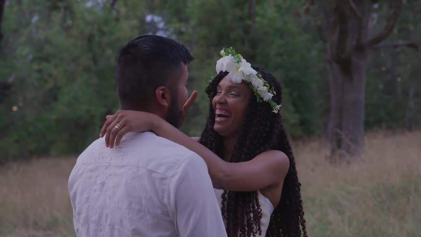 A woman wearing a wedding dress and a crown of flowers holds onto a man while she laughs