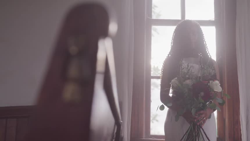 A bride stands in front of a window holding a bouquet