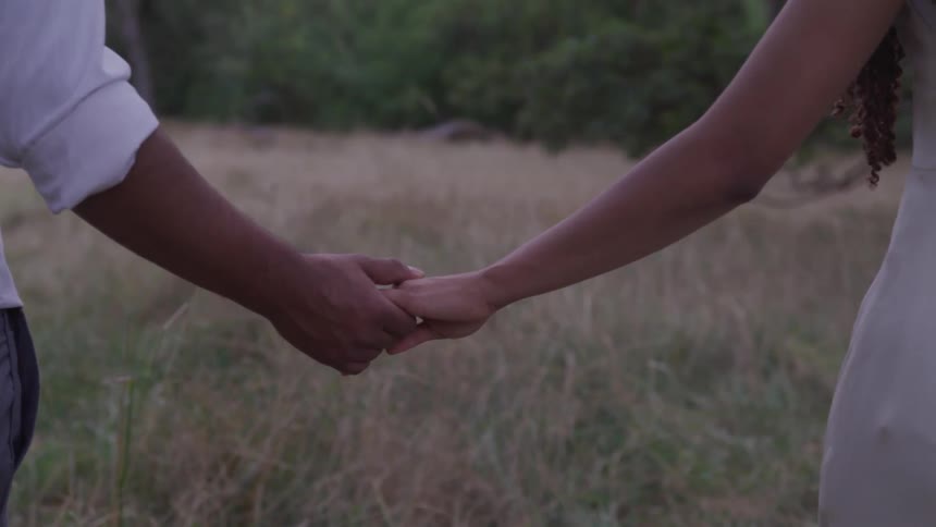 A black man and woman holding hands while walking through a field