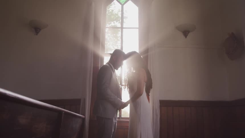 A bride and groom stand inside with their heads together