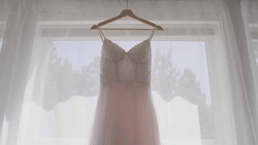 A wedding dress hanging in a window on the curtain rod