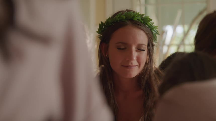 A young girls with leaves on her heads sits in a room with other girls with her eyes closed