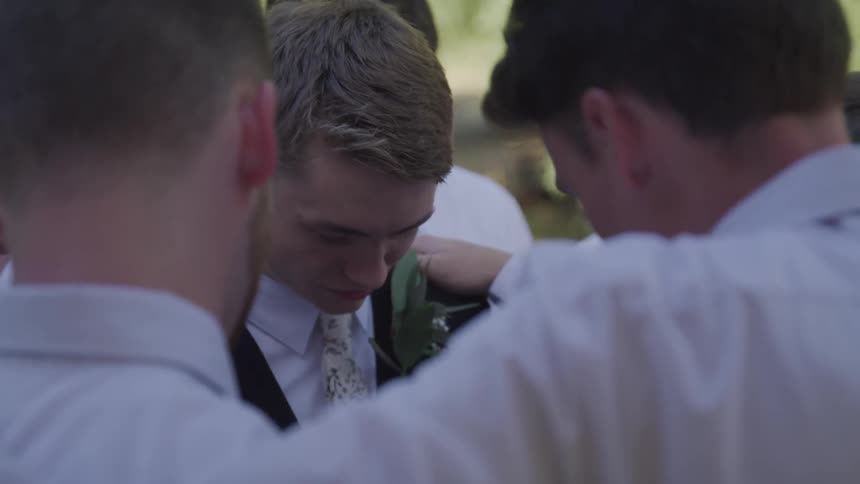 Group of men stand together in a circle with their heads bowed