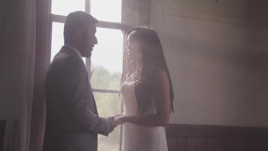 Newlyweds holding hands looking at each other in front of window