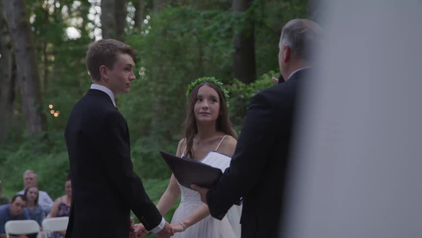 A bride and groom stand and hold hands in front of a minister