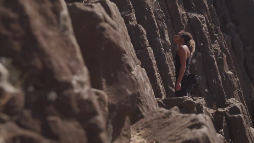 A woman stands at the base of a mountain staring up