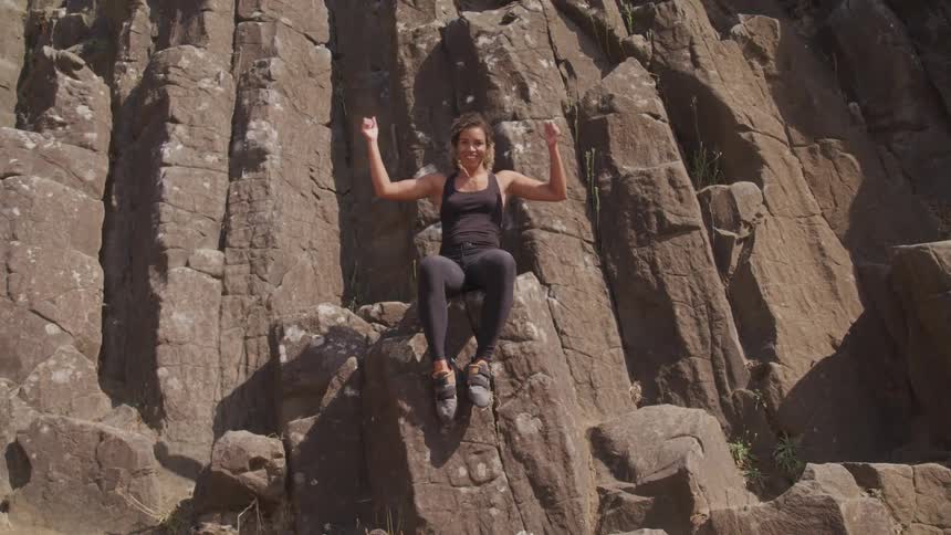 A woman sits on a mountain cliff and raises her arms in achievement