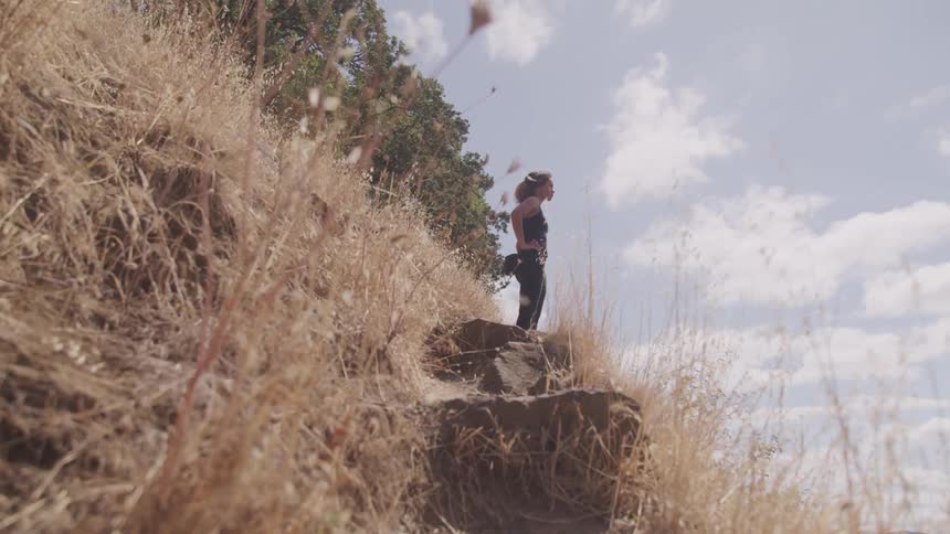 A young woman stands on a rock on a hill and looks across the land