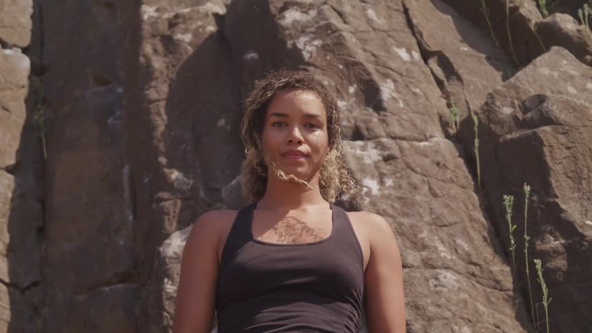 A woman stands in front of a rock wall